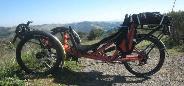 [photo: orange recumbent tricycle on Nimitz Way with Briones Hills in background]